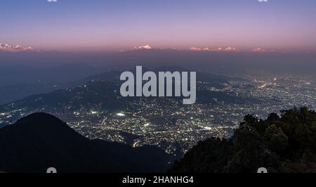 Ein Blick auf die Himalaya-Berge, die im Sonnenuntergang rosa leuchten und die Lichter, die in der Stadt Kathmandu, Nepal, aufleuchten. Stockfoto