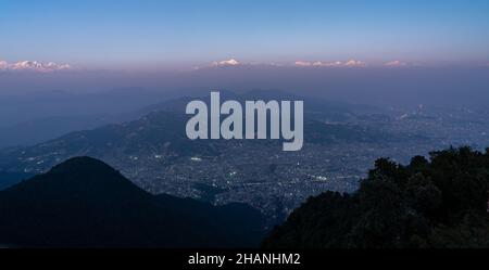 Ein Blick auf die Himalaya-Berge, die im Sonnenuntergang rosa leuchten und die Lichter, die in der Stadt Kathmandu, Nepal, aufleuchten. Stockfoto