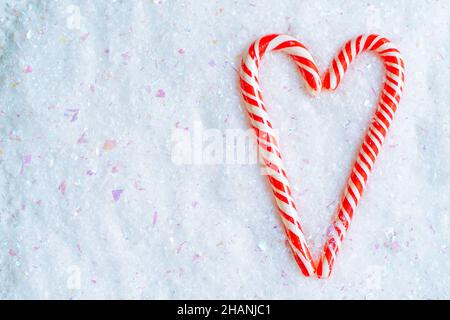 Zwei rote und weiße Zuckerstöcke bilden Herzform auf dem Schnee. Draufsicht Stockfoto