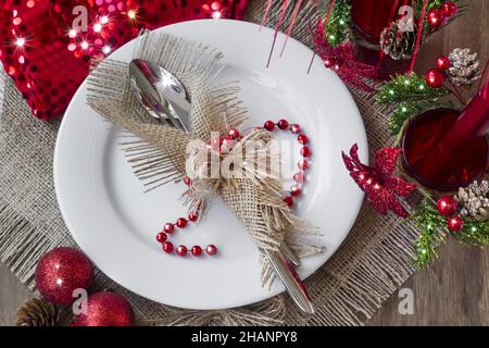 Stilvolles Besteck-Set in Jute-Serviette auf weißem Farbteller auf Quappe-Oberfläche mit weihnachtlichen Dekorationen eingewickelt Stockfoto