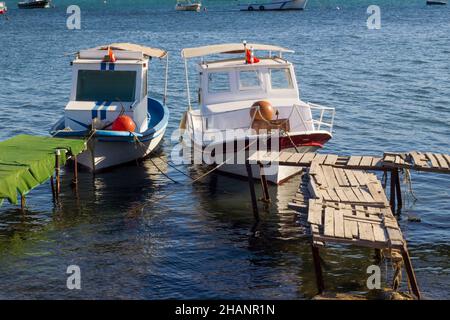 Zwei Fischerboote, die im Sommer auf dem hölzernen Pier im blauen Meer festgemacht sind Stockfoto