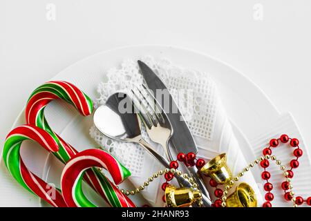 Traditioneller Weihnachtsteller mit stilvoller Stoffserviette, roter Kette, Glocke, Besteck-Set und Bonbonstöcken. Stockfoto