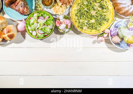 Festliches Abendessen, Osterbrunch. Traditionelle Ostergerichte auf dem Tisch der Familie - gebackenes Fleisch, Quiche, Frühlingsalat, Muffin, bunte Eier, Heiße Brötchen Stockfoto