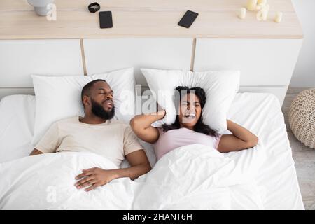 Unglücklich verzweifelt tausendjährige afroamerikanische Frau schreiend, bedeckt Ohren mit Kissen, leiden Schnarchen Stockfoto