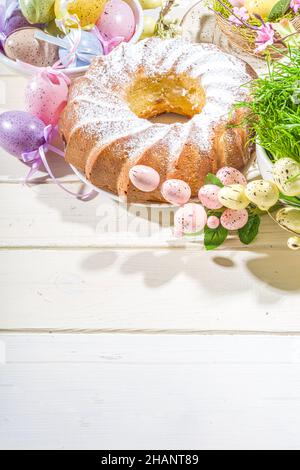 Traditionelle Frühlingsferien Osterrunde Kuchen mit Puderzucker gekrönt. Auf hellem Holzhintergrund mit Sonnenlicht, Ostereiern, Dekor und Frühlingszwirnholz Stockfoto