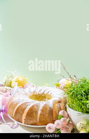 Traditionelle Frühlingsferien Osterrunde Kuchen mit Puderzucker gekrönt. Auf hellem Holzhintergrund mit Sonnenlicht, Ostereiern, Dekor und Frühlingszwirnholz Stockfoto