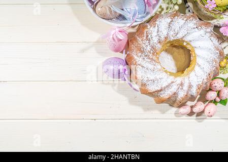 Traditionelle Frühlingsferien Osterrunde Kuchen mit Puderzucker gekrönt. Auf hellem Holzhintergrund mit Sonnenlicht, Ostereiern, Dekor und Frühlingszwirnholz Stockfoto