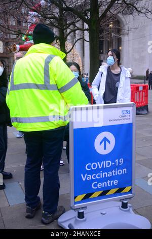Manchester, Großbritannien, 14th. Dezember 2021. Ein Mann in der Schlange von der Impfstelle des Rathauses sagt den Leuten in der Schlange, dass sie nicht genug Impfstoffe haben, um diejenigen in der Schlange hinter dem Zeichen im Bild zu impfen, und sie versuchen, mehr Impfstoffe zu erhalten. Im Rathaus in Manchester, England, Vereinigtes Königreich, warten sich Menschen für einen Auffrischungsimpfstoff zum Schutz vor Covid-19 oder Covid- oder Coronavirus an. Die britische Regierung hat ein Massenimpfungsprogramm gegen die Omicron Covid-Variante angekündigt. Quelle: Terry Waller/Alamy Live News Stockfoto