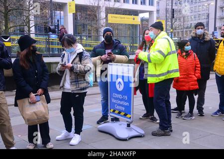 Manchester, Großbritannien, 14th. Dezember 2021. Ein Mann in der Schlange von der Impfstelle des Rathauses sagt den Leuten in der Schlange, dass sie nicht genug Impfstoffe haben, um diejenigen in der Schlange hinter dem Zeichen im Bild zu impfen, und sie versuchen, mehr Impfstoffe zu erhalten. Im Rathaus in Manchester, England, Vereinigtes Königreich, warten sich Menschen für einen Auffrischungsimpfstoff zum Schutz vor Covid-19 oder Covid- oder Coronavirus an. Die britische Regierung hat ein Massenimpfungsprogramm gegen die Omicron Covid-Variante angekündigt. Quelle: Terry Waller/Alamy Live News Stockfoto