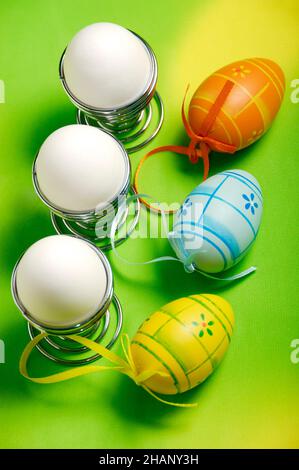 Kolofulige Ostereier und weiße Eier in Silbereier stehen mit fröhlichen Bändern auf fröhlichem frühlingsgrünen gelben Hintergrund Stockfoto
