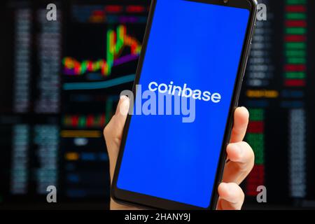Ukraine, Odessa - Oktober, 9 2021: Hand hält Handy mit Coinbase App läuft auf Smartphone-Bildschirm mit Trading-Seite im Hintergrund. Coinbase ist Ame Stockfoto
