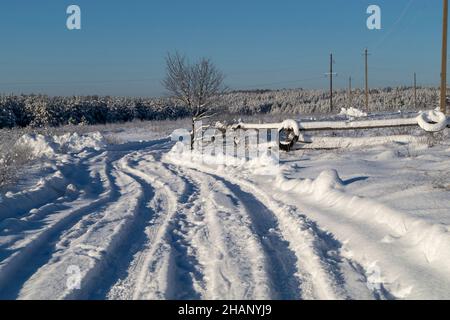 Winterstraße durch ein Feld im Dorf. Schöne Landschaft auf dem Land gegen den blauen Himmel Stockfoto