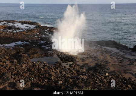 Eine Wasserwolke, die durch ein Blowhole auf einem vulkanischen Schelf im Spouting Horn Beach Park am Südufer von Kauai, Hawaii, aufkommt Stockfoto