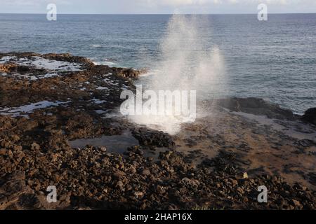 Wassertröpfchen, die nach dem Auftauchen durch ein Blowhole auf einem vulkanischen Schelf im Spouting Horn Beach Park am Südufer von Kauai, Hawaii, herabfallen Stockfoto