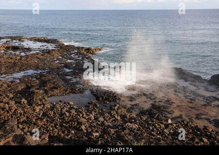 Wassertröpfchen, die nach dem Auftauchen durch ein Blowhole auf einem vulkanischen Schelf im Spouting Horn Beach Park am Südufer von Kauai, Hawaii, herabfallen Stockfoto