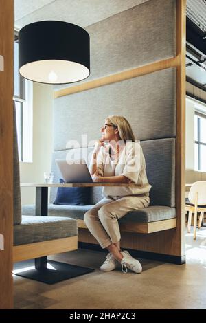 Besinnliche reife Geschäftsfrau, die in einem modernen Arbeitsraum arbeitet. Reife Geschäftsfrau, die an neue Geschäftsideen denkt. Erfahrene Unternehmerin Stockfoto