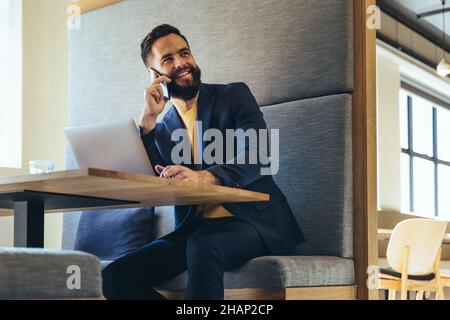 Glücklicher junger Geschäftsmann, der telefoniert. Fröhlicher junger Geschäftsmann, der lächelt, während er mit seinen Geschäftspartnern kommuniziert. Erfolgreiche Entrep Stockfoto