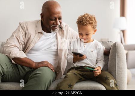 Schwarzer Großvater Und Kleiner Enkel Benutzen Zu Hause Das Handy Zusammen Stockfoto