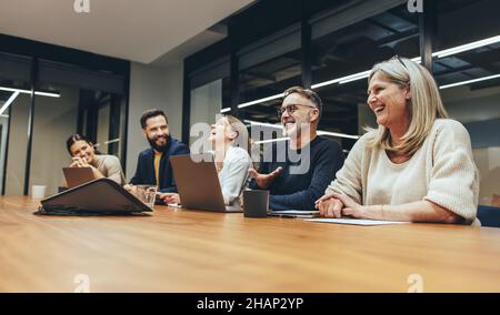 Fröhliche Geschäftsleute, die während einer Sitzung in einem Sitzungssaal lachen. Team aus verschiedenen Geschäftsleuten, die gerne in einer modernen Arbeitswelt zusammenarbeiten Stockfoto