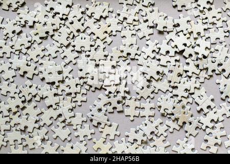 Viele hellgraue strukturierte Puzzleteile aus Pappe auf einem Tisch, Wochenend-Indoor-Aktivitäten zum Spielen mit Kindern zu Hause Stockfoto