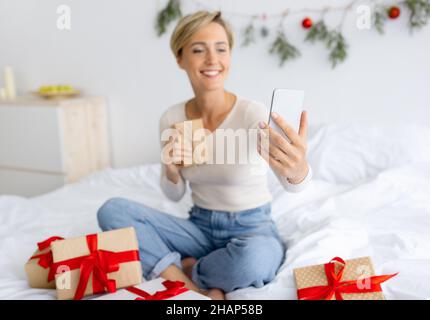 Lady mit Handy macht Videocall auf Weihnachten halten Geschenk Stockfoto