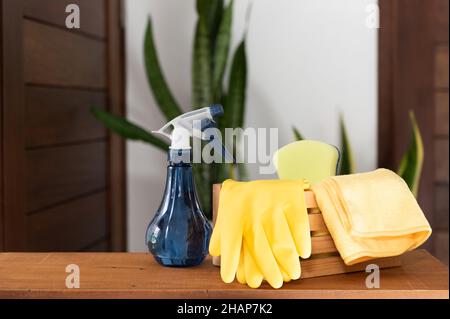 Korb mit Reinigungsmitteln auf Holztisch im Haus mit grünem Sanseviera laurentii Pflanze Hintergrund Stockfoto