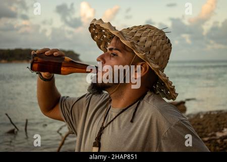 Ein erwachsener Mann mit Hipster oder Hippie sieht während des Sonnenuntergangs beim Bier am Strand aus. Reisende, die den Moment genießen. Stockfoto