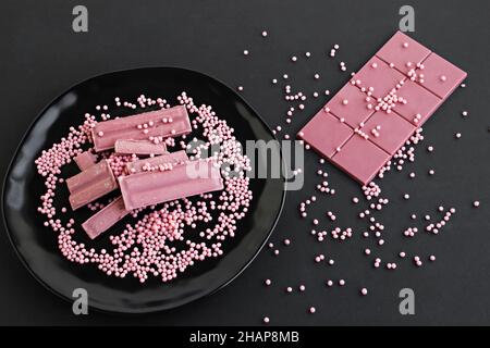 Die vierte Art von Schokolade: Rubinschokolade ist auf schwarzem Porzellanteller mit Dekoration Bonbons.Draufsicht, schwarze Oberfläche. Stockfoto