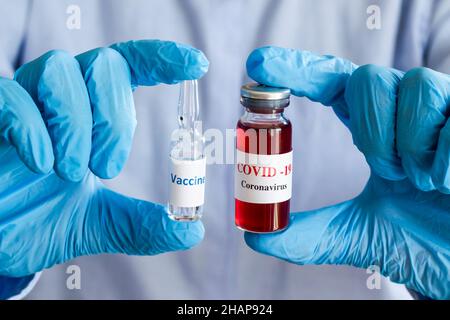 Blaue Hand mit Handschuhen hält Mini-Flasche Medizin, Impfstoff und es sagt Covid - 19, Coronavirus und Impfstoff auf den Flaschen. Konzeptionelles Bild der medizinischen sec Stockfoto