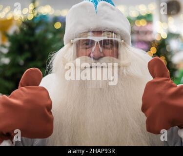 Das Porträt des russischen weihnachtsmanns mit einem Schutzvisier zeigt die Daumen nach oben. Stockfoto