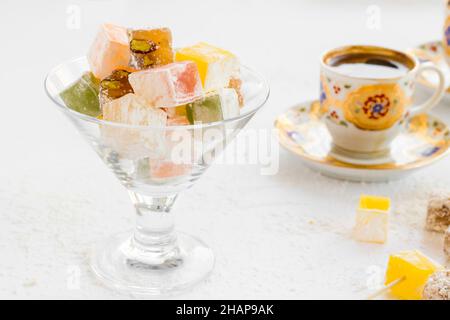 Traditionelle türkische Delicious Delight Lokum, in Glas-Süßigkeitenschale auf weißer Oberfläche mit verschwommenem Kaffee.Konzeptbild des Zuckerfestes Stockfoto