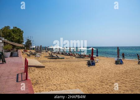 Der wunderschöne weiße Sandstrand von Griechenland mit leeren Sonnenliegen und Sonnenschirmen ist wunderschön. Türkisfarbenes Meerwasser und blauer Himmel. Griechenland. Stockfoto