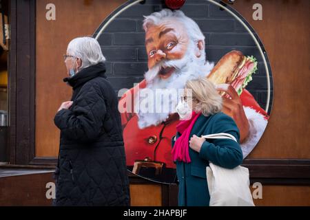Da die Anzahl der Omicron Covid-Variantenfälle in Großbritannien zunimmt und die Beschränkungen des Plans B der Regierung im Vorfeld von Weihnachten andauern, laufen die Öffentlichkeit, die Gesichtsbedeckungen trägt, am 14th. Dezember 2021 in London, England, an einem Bild des Weihnachtsmannes auf dem Trafalgar Square vorbei. Stockfoto