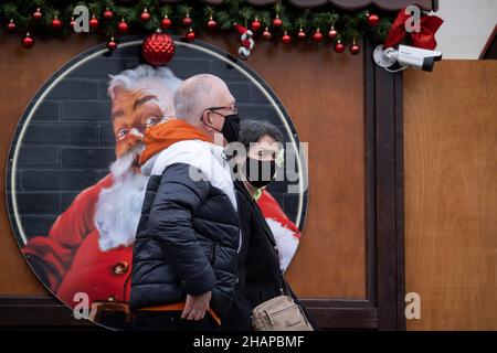 Da die Anzahl der Omicron Covid-Variantenfälle in Großbritannien zunimmt und die Beschränkungen des Plans B der Regierung im Vorfeld von Weihnachten andauern, laufen die Öffentlichkeit, die Gesichtsbedeckungen trägt, am 14th. Dezember 2021 in London, England, an einem Bild des Weihnachtsmannes auf dem Trafalgar Square vorbei. Stockfoto