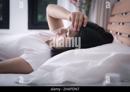 Asiatische Frau bekommen Kopfschmerzen und Kälte im Bett liegend, um besser zu werden, gesund und Medizin Konzept Stockfoto