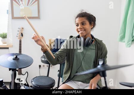 Happy niedlich biracial Schulmädchen mit Drumsticks schlagen Trommeln bei der Lektion der Musik in häuslicher Umgebung Stockfoto
