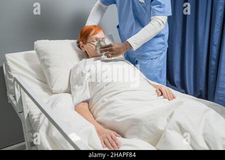 Uniformierte Ärztin, die einer älteren Frau eine Sauerstoffmaske auflegt, während sie in einer Krankenhausabteilung im Bett liegt Stockfoto