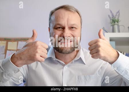 Mann mittleren Alters zeigt Daumen nach oben in homa Büro. Online-Anrufkonzept Stockfoto