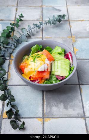 Köstliches Frühstück, Brunch - pochiertes Ei, Lachs, Avocado, Rukula-Salat auf gefliestem Hintergrund Stockfoto