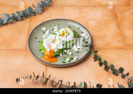 Grüne Erbsen mit pochierten Eiern auf sandfarbenem Hintergrund Stockfoto