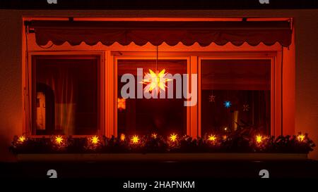 Strahlender, strahlender Weihnachtsstern im Fenster einer Nacht. Traditionelle Einrichtung der Weihnachtszeit mit Blick auf einen beleuchteten Balkon. Stockfoto