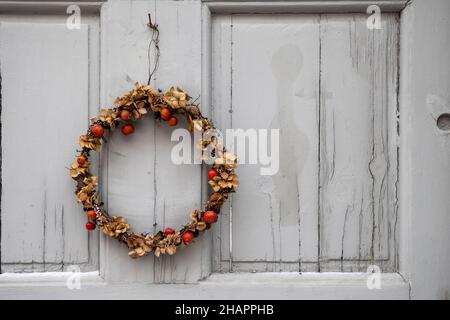 Weihnachtskranz im skandinavischen Stil aus getrockneten Pflanzen und Beeren, der während der Weihnachts- und Neujahrsferien in Schweden an der grauen Tür hängt. Stockfoto