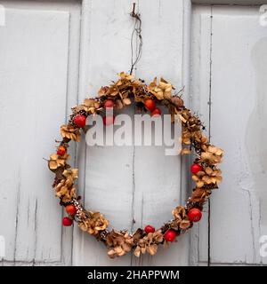 Weihnachtskranz im skandinavischen Stil aus getrockneten Pflanzen und Beeren, der während der Weihnachts- und Neujahrsferien in Schweden an der grauen Tür hängt. Stockfoto