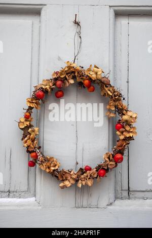 Weihnachtskranz im skandinavischen Stil aus getrockneten Pflanzen und Beeren, der während der Weihnachts- und Neujahrsferien in Schweden an der grauen Tür hängt. Stockfoto