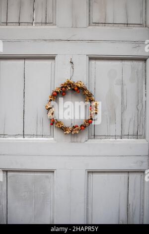 Weihnachtskranz im skandinavischen Stil aus getrockneten Pflanzen und Beeren, der während der Weihnachts- und Neujahrsferien in Schweden an der grauen Tür hängt. Stockfoto