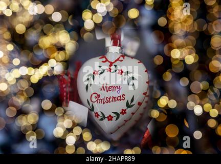 Weißrussland, Minsk - 18. Oktober 2021 Frohe Weihnachten Text über herzförmiges Spielzeug mit verschwommenem Licht der Weihnachtsfeiertage Girlande. Stockfoto
