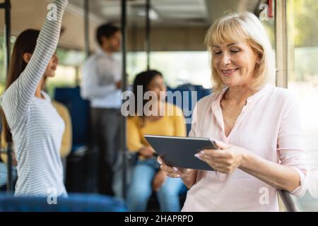 Porträt einer lächelnden älteren Frau, die mit dem Tablet in den Bus fährt Stockfoto