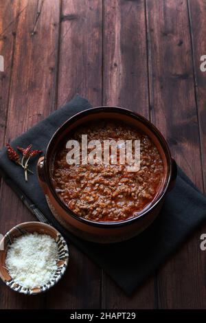 Hausgemachte Bolognese- oder ragù-Sauce in rustikaler Schüssel, auf dunklem Holz serviert. Direkt darüber. Stockfoto