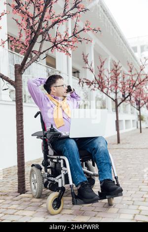 Ein Mann mit Behinderungen im Rollstuhl, der auf einem Smartphone spricht Stockfoto