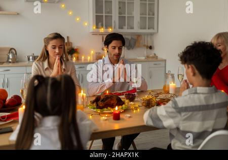 Große Familie mit mehreren Generationen, die vor dem Weihnachtsessen zu Hause am Tisch betet Stockfoto